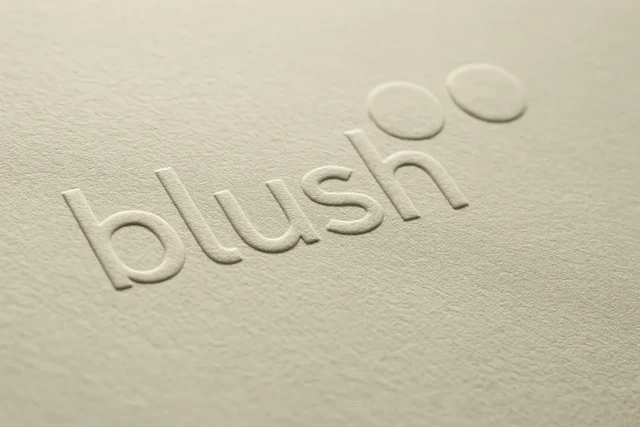Close-up of the word "blush" embossed on soft off-white textured paper, showing raised letters and smooth shadows for a clean, premium look