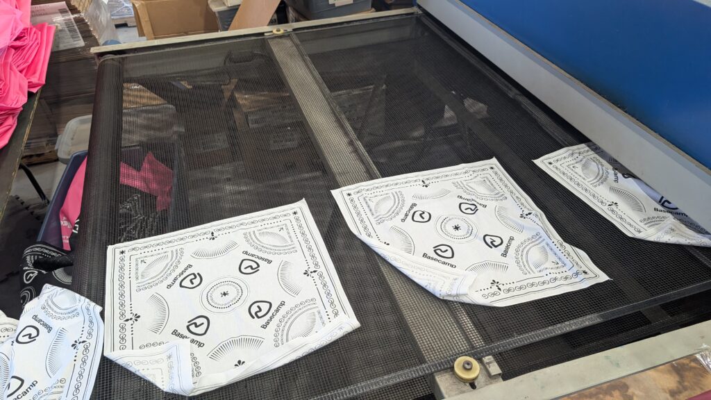 White customizable bandanas with printed designs moving through a production dryer.