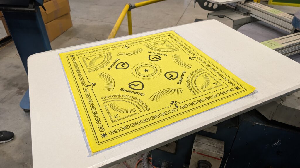 Yellow customizable bandana with black printed design on a production table.