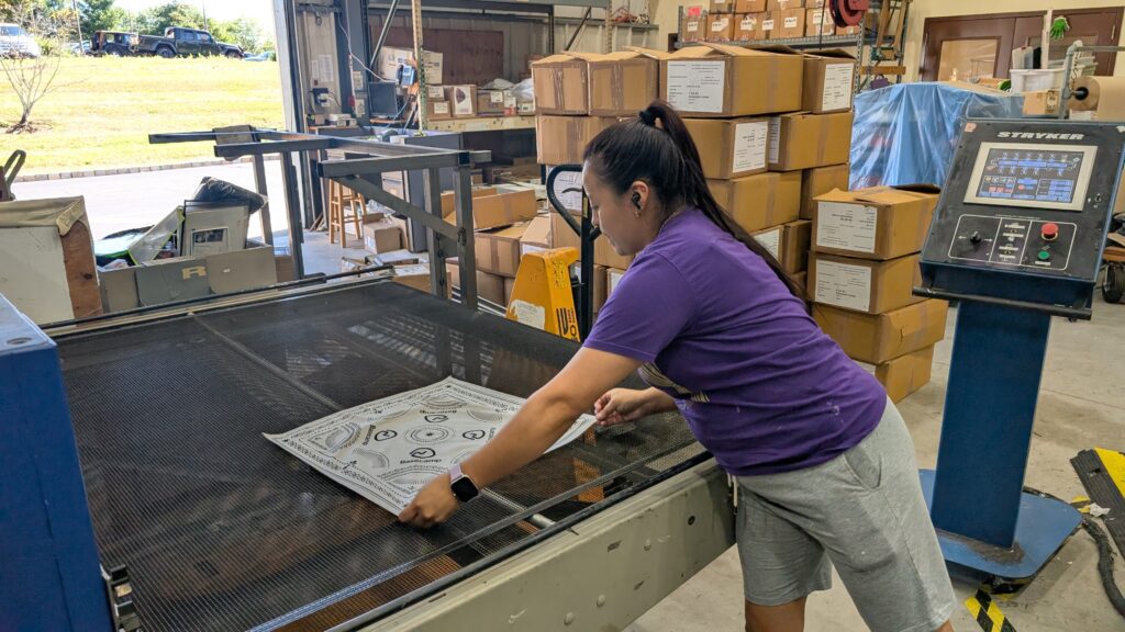 Worker positioning a customizable bandana on screen printing equipment during production.