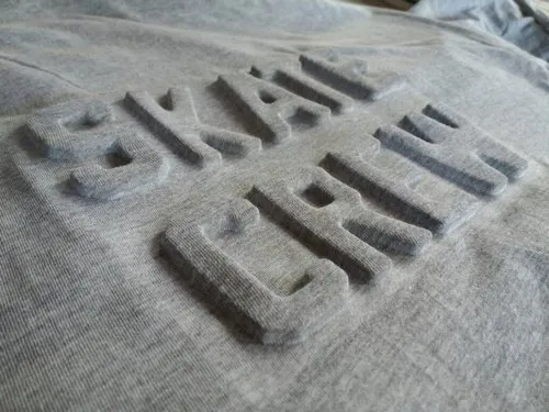 Close-up of a gray T-shirt with a bold debossed “SKATE CREW” design embossed into the fabric.