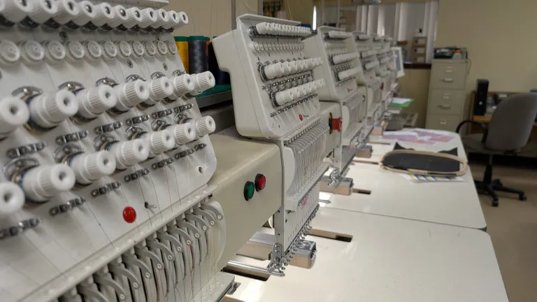 Professional Tajima embroidery machine stitching a Dog Walker hat design with multiple thread colors loaded.