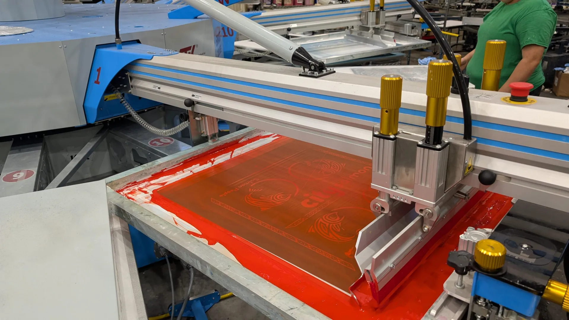 Automated screen printing press applying vibrant red ink to custom bandanas at AMBRO Manufacturing for Canadian clients