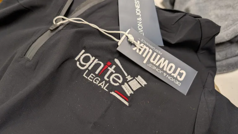 Black Devon & Jones quarter-zip pullover with an embroidered Ignite Legal logo and attached brand tag.