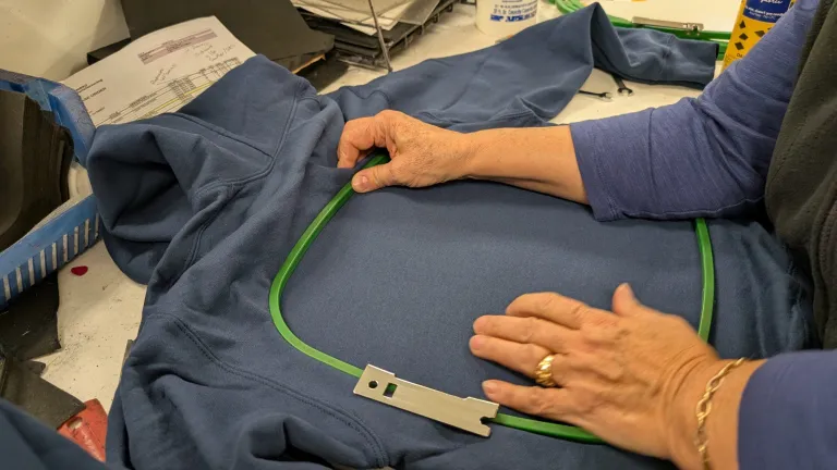 Hands hooping a navy hoodie with a green embroidery frame during setup in a production workspace.