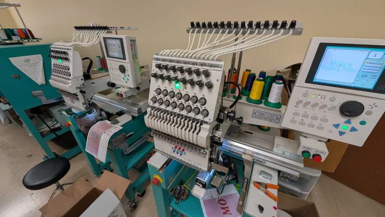 Two Tajima embroidery machines operating in a production shop with colorful thread cones and active embroidery designs on the screens.
