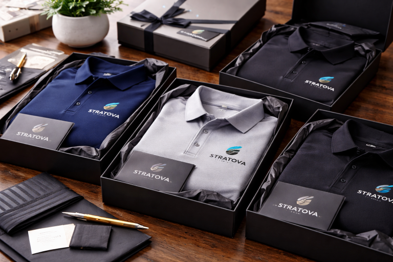 Custom embroidered polo shirts in navy gray and black displayed inside premium black gift boxes with branded cards in landscape format.