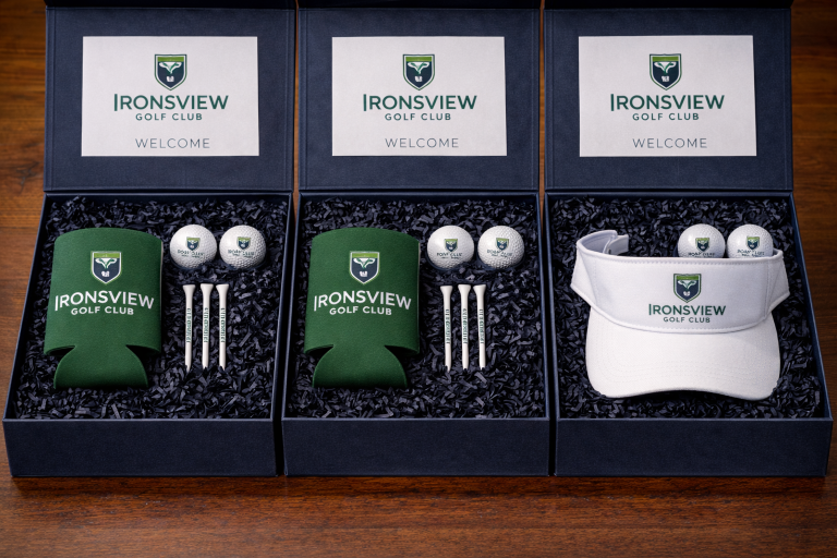 Golf event welcome kit with Ironsview Golf Club branded golf balls, tees, beer koozie, and embroidered visor in navy box