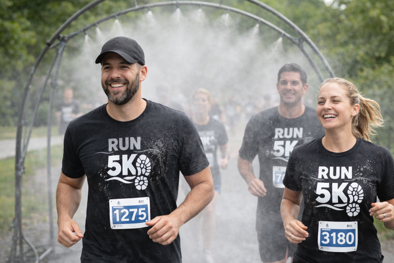 5K runners wearing black shirts with white hydrochromic logos appearing as they run through a misting arch